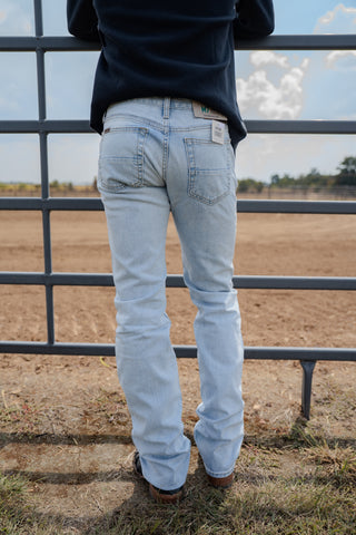 Person wearing light blue jeans standing behind a metal fence with a field and sky in the background.