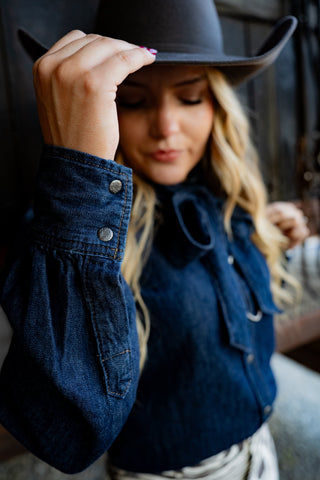 Woman wearing a denim jacket and cowboy hat, looking down.