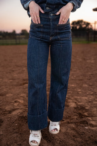Person wearing blue jeans standing on a dirt field with a blurred background
