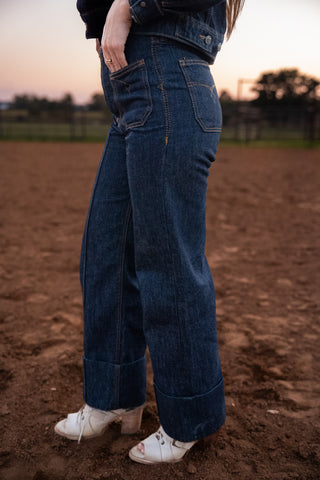 Person wearing blue jeans standing on a dirt field with a blurred background