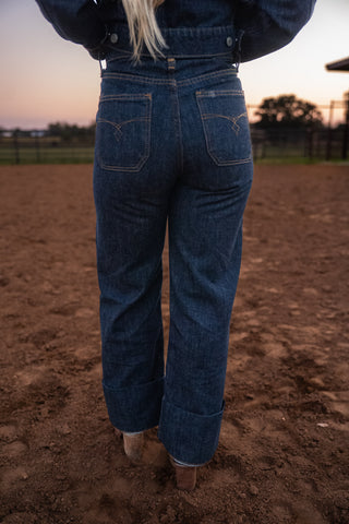 Person wearing blue jeans standing on a dirt field with a sunset in the background