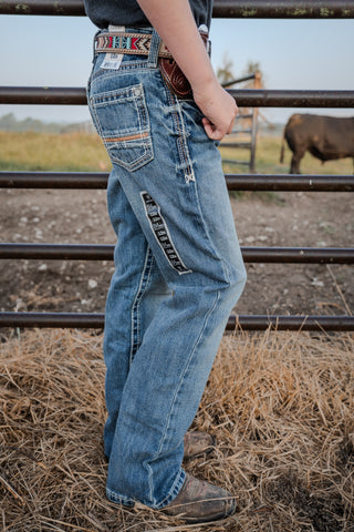 Person wearing blue jeans with a belt and cow in the background