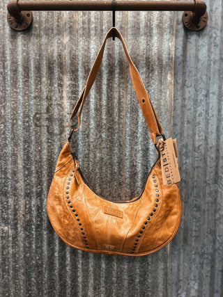 Brown leather handbag with studded details hanging on a metal wall.