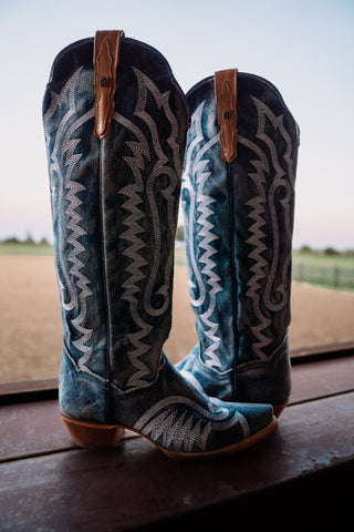 Pair of blue and black cowboy boots with intricate designs on a wooden surface.