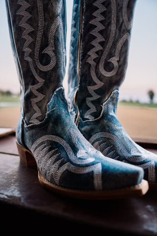 Blue cowboy boots with intricate white patterns on a wooden surface.