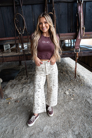 Woman standing in a stable wearing a maroon crop top and patterned pants.