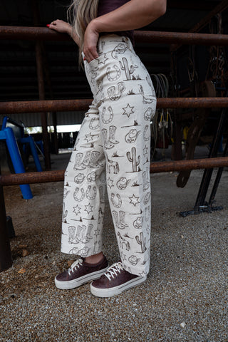 Person wearing white pants with black patterns, standing in a rustic setting.