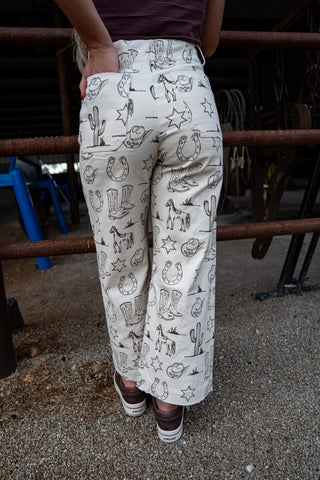 Person wearing patterned pants with cowboy graphics in an outdoor setting.
