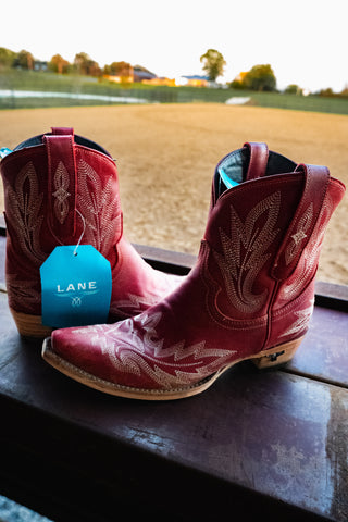 Red cowboy boots with a visible 'Lane' tag on a window sill with a view of a field.