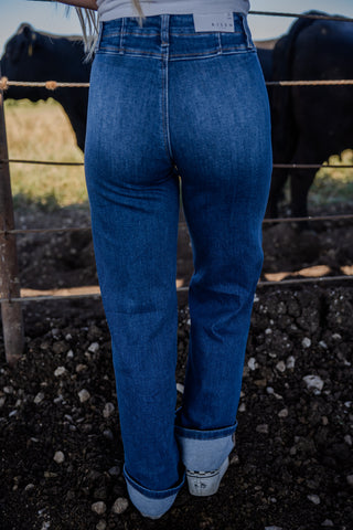 Person wearing blue jeans standing in front of a fence with animals in the background