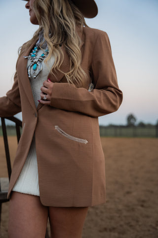 Woman wearing a brown blazer over a white dress in an outdoor setting