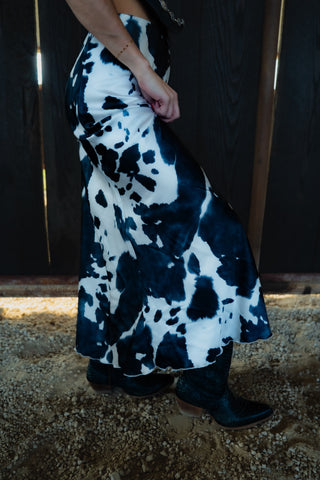 Person wearing a black and white patterned dress with boots on a textured surface.