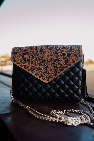 Black quilted handbag with floral embossing on a reflective surface