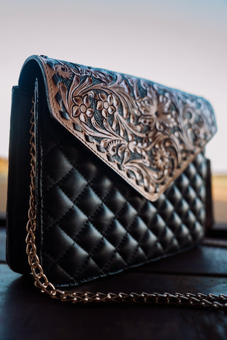 Black quilted handbag with intricate leather flap on a wooden surface