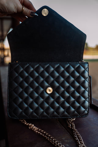 Black quilted handbag with gold chain strap held by a hand.