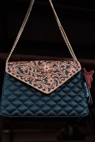 Blue quilted handbag with floral embossing and chain strap on a dark background