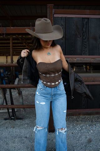 Person wearing a cowboy hat, brown top, and blue jeans in an indoor setting.