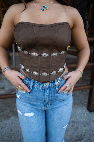 Person wearing a brown corset with silver embellishments and blue jeans.