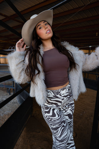 Woman wearing a fur coat, brown top, and zebra print pants in an indoor setting.