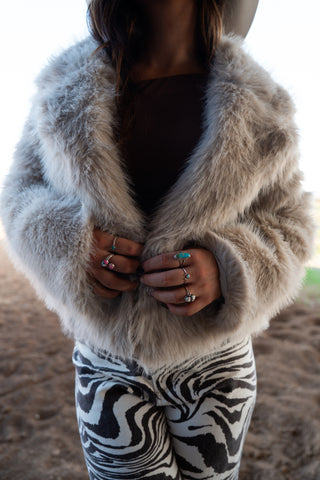Person wearing a fluffy gray coat and zebra-patterned pants with a blurred background