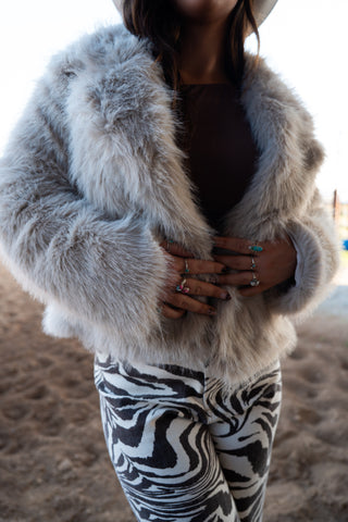 Person wearing a fluffy gray coat and zebra print pants on a blurred background