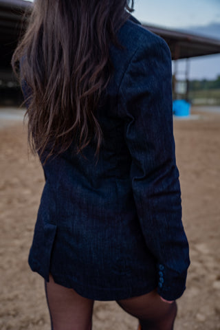 Person wearing a dark blue blazer with long hair, standing on a sandy surface.