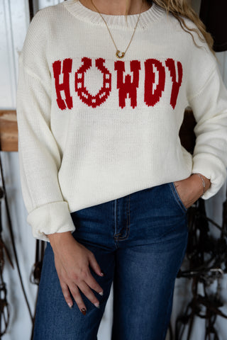 Person wearing a white sweater with 'HOWDY' printed in red, paired with blue jeans.
