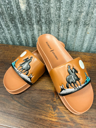 Pair of tan slides with horse design on a wooden surface