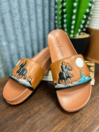Brown sandals with horse design on a wooden surface with a plant in the background