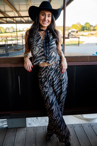 Woman in zebra print outfit and black hat standing on a wooden platform.