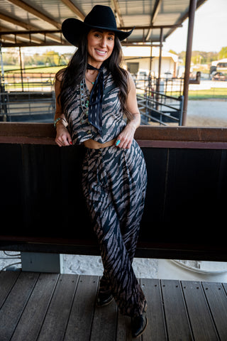 Woman in a zebra print outfit and cowboy hat leaning against a railing.