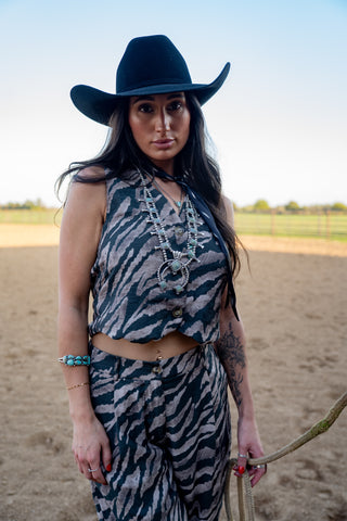 Woman in zebra print outfit and cowboy hat holding a rope in an outdoor setting