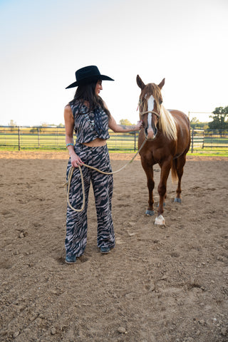 Woman in zebra print outfit and cowboy hat standing next to a horse in an outdoor setting