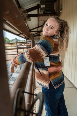 Woman wearing a colorful striped sweater and blue jeans, standing next to a horse.