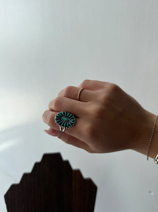 Hand wearing a ring with a green gemstone on a neutral background