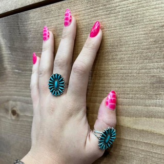 A person's hand displaying two sterling silver rings with turquoise stones on the fingers.