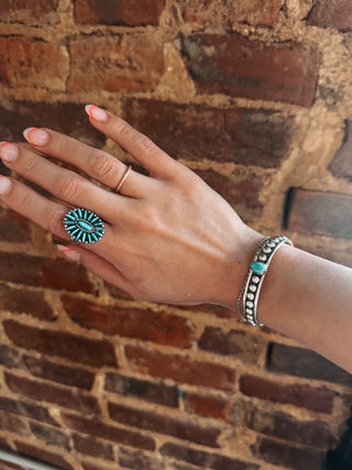 Hand wearing a turquoise ring and bracelet against a brick wall
