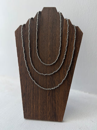 Three beaded necklaces on a wooden stand against a white background