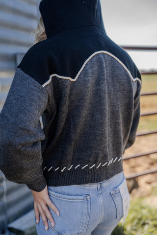 Person wearing a black and gray patterned sweater with a hood, standing outdoors.