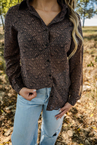 Person wearing a brown patterned shirt and light blue jeans in an outdoor setting with trees and grass.