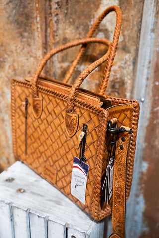 Brown leather handbag with braided handles on a wooden surface