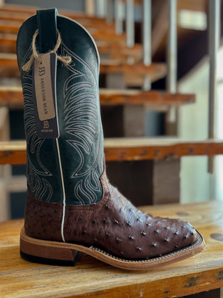 Brown cowboy boot with green uppers on a wooden surface