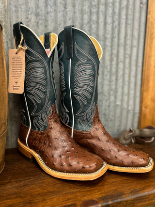 Pair of cowboy boots with a brown sole and green uppers on a wooden surface.