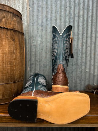 Pair of cowboy boots with a wooden barrel and metal wall in the background