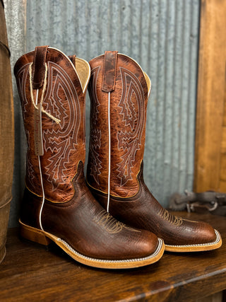 Pair of brown leather cowboy boots with intricate designs on a wooden surface.