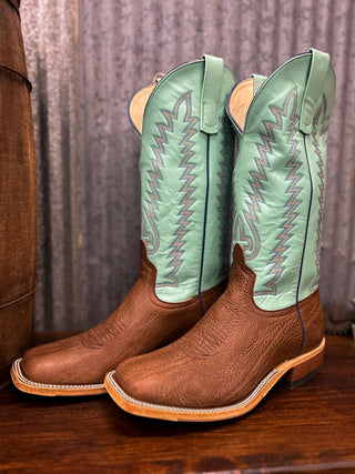 Pair of brown cowboy boots with green tops on a wooden surface.