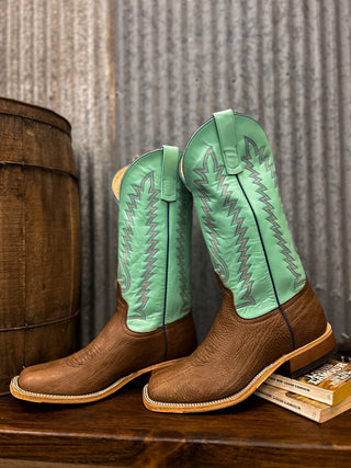 Pair of brown and green cowboy boots on a wooden surface with a rustic background.