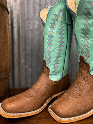 Pair of brown and green cowboy boots with detailed stitching on a wooden surface.