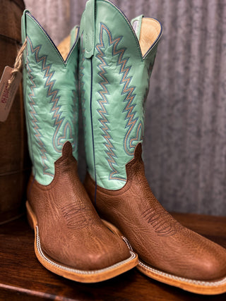 Pair of brown cowboy boots with green uppers on a wooden surface.