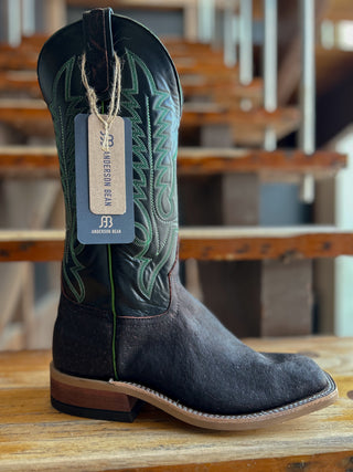 Black cowboy boot with green stitching on a wooden surface, brand tag visible